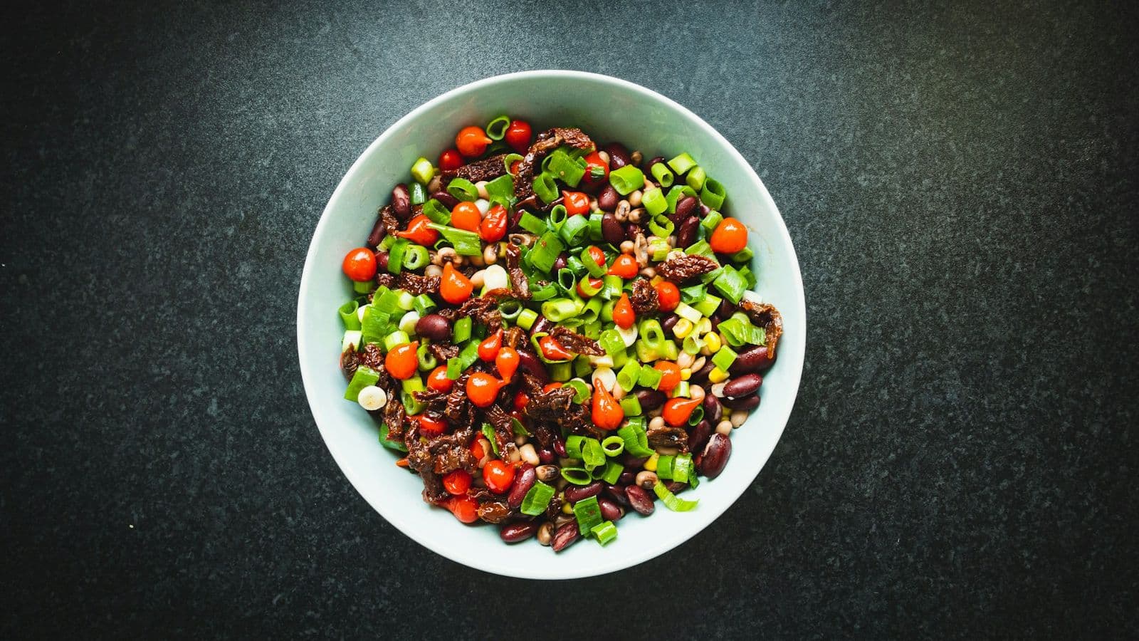 Bønnesalat med tomat, vårløk og mais i en hvit skål på mørk bakgrunn