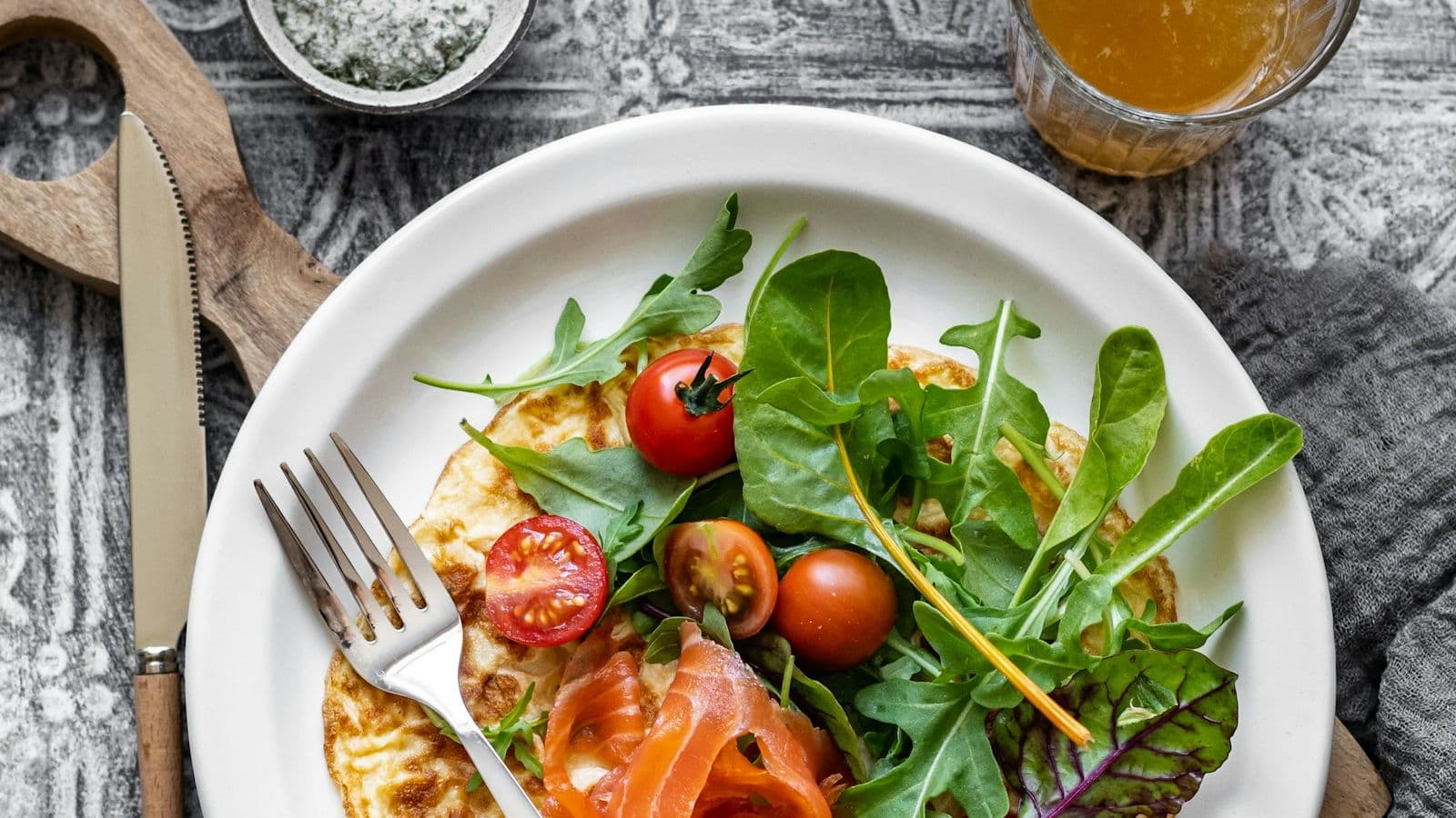 Omelett med røkt laks, tomater og salat på en hvit tallerken