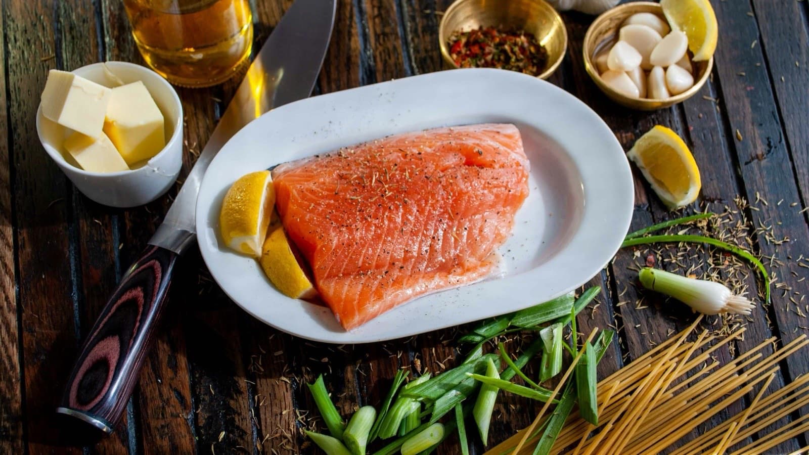 Rå laksefilet med sitronbåter på et hvitt fat, omgitt av smør, hvitløk og vårløk